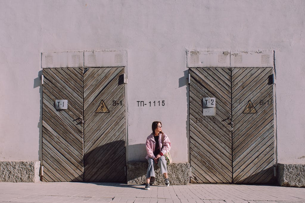 Full body of peaceful female sitting between shabby wooden doors in sunny day